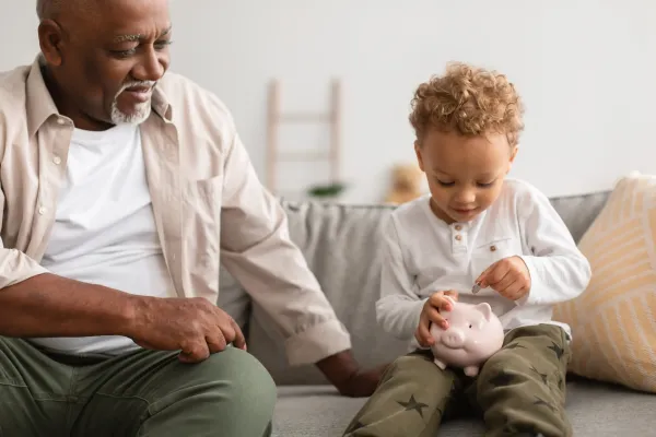 A grandfather and grandchild placing coins in a piggy bank